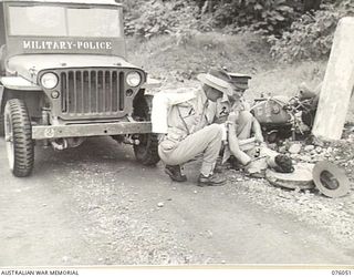 LAE, NEW GUINEA. 1944-09-21. A MEMBER OF THE NEW GUINEA FORCE PROVOST COMPANY, SERGEANT H.H. BURNISTON (1) RENDERING AID TO AN INJURED DESPATCH RIDER, CORPORAL L. BYRNE (3). IDENTIFIED PERSONNEL ..