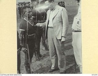 BISIATABU, NEW GUINEA. 1944-04-19. THE HONOURABLE E.J. WARD, MINISTER FOR EXTERNAL TERRITORIES IN THE AUSTRALIAN GOVERNMENT (2), EXAMINES A LOYAL SERVICE MEDAL WORN BY CORPORAL AIWAI (1), WATCHED ..