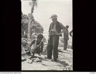 KIRIWINA, TROBRIAND ISLANDS, PAPUA. 1944-01-31. AIRCRAFTMAN 1 A. R. HILL OF MONTO, QLD (RIGHT), HAS BEEN ADOPTED AS FRIEND BY LOCAL NATIVE KATULOKA, WHO IS SHOWN CARVING UP A COCONUT FOR HIS RAAF ..