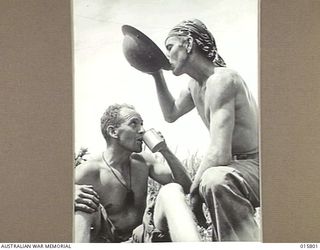 1943-09-25. NEW GUINEA. FALL OF LAE. PTE. E. MACDONALD OF PERTH, W. AUST., DRINKS OUT OF A TIN AND PTE. D. DOONAN OF BONDI, N.S.W. OUT OF HIS TIN HAT DURING A REST AT LAE