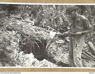 SATTELBERG AREA, NEW GUINEA. 1943-11-18. SX14068 PRIVATE L. W. STILES OF THE 2/48TH AUSTRALIAN INFANTRY BATTALION EXAMINING A JAPANESE MORTAR IN FRONT OF A JAPANESE DUGOUT DURING A LULL IN THE ..