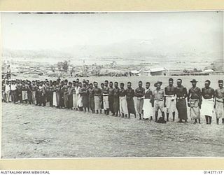 1943-03-03. NATIVE CARRIERS WHO WATCHED PRESENTATION OF LOYAL SERVICE MEDALS TO FOUR CONSTABLES, AT WAU AERODROME, WERE A COLOURFUL GROUP. SOME OF THEM WORE THEIR LAP LAPS OF BRIGHT COLOURED COTTON ..