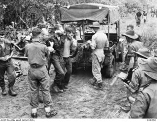 Aitape Sector, New Guinea. March 1945. Being helped to a jeep-ambulance on a forward track near Sowam is wounded soldier NX32941 Private J.J. Parkes, 10 Platoon, B Company, 2/2nd Infantry ..