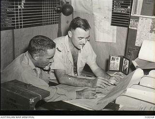 VIVIGANI, GOODENOUGH ISLAND, PAPUA NEW GUINEA. C. 1943-09. FLYING OFFICER A. GILBERT OF BELLEVUE HILL, NSW (RIGHT), DISCUSSING A PLAN WITH FO J. W. MCENIRY OF MILDURA, VIC, IN THE OFFICE OF NO. 7 ..