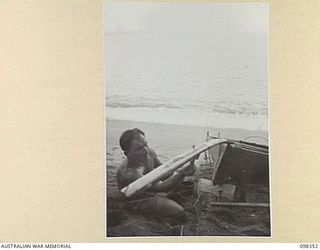 WEWAK, NEW GUINEA. 1945-10-28. PRIVATE J. HALVER, 16 INFANTRY BRIGADE, PAINTING THE BOWSPRIT OF THE SKIFF, SLIM, AN ENTRY IN THE WEWAK REGATTA TO BE HELD IN DALLMAN HARBOUR ON SUNDAY 11 NOVEMBER ..