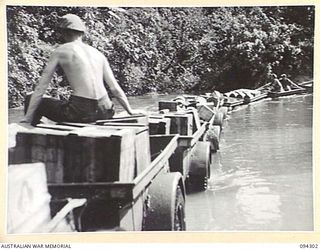 BOUGAINVILLE. 1945-07-21. TRAILERS OF 29 INFANTRY BRIGADE LOADED WITH RATIONS AND TOWED BY A TRACTOR TRAIN, FLOAT ACROSS THE OGORATA RIVER. THE RIVER IS FLOODED DUE TO THE HEAVY RAINFALL