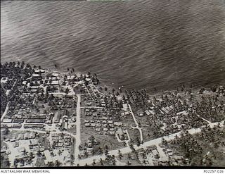Madang, New Guinea, 1945-10. Aerial view of Headquarters, RAAF Northern Command (NORCOM), on the shores of Madang Harbour. Buildings and tents are neatly laid out in groups among tall palm trees ..