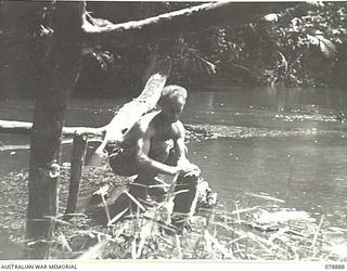 BOUGAINVILLE ISLAND. 1945-02-03. VX115812 PRIVATE A.T. SHUGG, "A" COMPANY, 9TH INFANTRY BATTALION WASHING HIS CLOTHES ON A LOG JUTTING OUT INTO THE HUPAI RIVER NEAR MAWARAKA