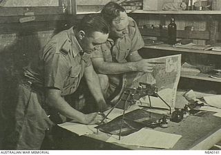 Two RAAF Intelligence Officers, 255538 Flying Officer (FO) Harold Peter Moschetti (left) and 255266 FO Stuart Patrick King, examine aerial photographs of the Japanese-held Kahili airstrip on ..