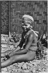 Adolescent girl, Kena, with talcum powder around her eyes, and marsupial fur cap, smiling while sitting near Cooks' Kwiop house