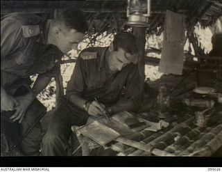 Saigora, New Guinea. 1945-08-05. NX69 Lieutenant Colonel P.K. Parbury, Commanding Officer, 2/7th Australian Infantry Battalion, seated, and VX3829 Major H. Laver, Second in Command, studying a map ..