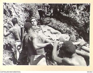 BOUGAINVILLE, 1945-05-18. PRIVATE W.J. BARRET, B COMPANY, 57/60 INFANTRY BATTALION, WOUNDED IN THE ACTION IN THE ADVANCE ALONG THE AXIS OF COMMANDO ROAD, IS CARRIED BACK BY NATIVES ALONG A TRACK ..
