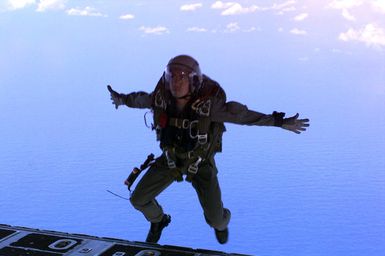 Straight on medium shot of US Marine GUNNERY Sergeant Longnecker, Jumpmaster, 5th Force Reconnaissance Battalion, 3rd Marine Division, as he jumps from the rear entrance of a USAF C-130 Hercules Cargo aircraft with its MC5 Freefall Square Parachute 9-thousand feet above Andersen Air Force Base during Force Reconnaissance Exercises