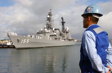 A US Navy (USN) Sailor assigned to the line handling crew at Naval Station Pearl Harbor, Hawaii (HI), watch as the Japanese Maritime Self-Defense Force (JMSDF), ASAGIRI CLASS: Destroyer, HAMAGIRI (DD 155), commences docking procedures with the assistance of a commercial harbor tug boat, as the ship arrives at Pearl Harbor, HI