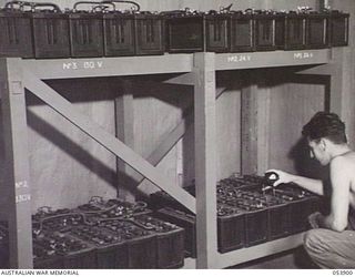 PORT MORESBY, NEW GUINEA. 1943-07-14. VX103270 CORPORAL H. O'CONNOR CHECKING BATTERIES ON RACKS USED FOR CARRIER SYSTEM DURING CHARGING