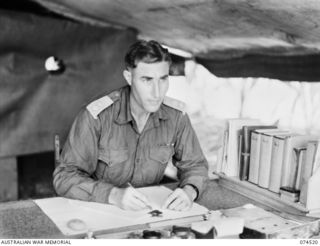 MATUPI, NEW GUINEA. VX220 Lieutenant-Colonel William Dudley Refshauge, OBE, Commanding Officer, 15th Field Ambulance at work in his office. The three volumes on the shelf are the brown paper ..