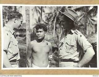 MILNE BAY, NEW GUINEA. 1943-06-26. QX43433 SIGNALMAN L.J. CALLEN (LEFT) AND Q46579 PRIVATE H.J. SMITH WITH NATIVE BOY, WILLIAM, WHO WORKS AS A RUNNER FOR THE SIGNALS SECTION, HEADQUARTERS, 5TH ..