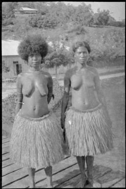 Two Papuan women wearing grass skirts standing on a jetty, Papua, ca. 1923 / Sarah Chinnery