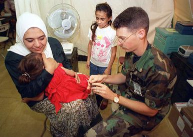 US Air Force SENIOR AIRMAN (SR) Joseph Siddall, 374th Air Transportation Hospital, Yokota, Japan, administers immunization shots to Kurdish evacuees at Andersen Air Force Base, Guam, during OPERATION PACIFIC HAVEN. Pacific Haven, a joint humanitarian effort conducted by the U.S. Military, airlifted over 2100 Kurdish refugees from northern Iraq. The Refugees will be housed temporarily at Andersen AFB, Guam, while they go through the immigration process for residence into the United States