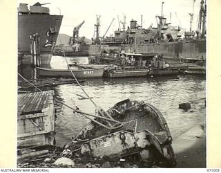 LAE, NEW GUINEA. 1944-03-09. A GENERAL VIEW OF THE WHARVES SHOWING A WRECKED JAPANESE BARGE BEACHED IN THE FOREGROUND. PINNACES AND BARGES ARE IN THE CENTRE OF THE PICTURE WITH LARGE SHIPS ..