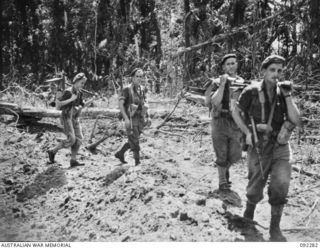 BOUGAINVILLE. 1945-05-17. MEMBERS OF C COMPANY, 57/60 INFANTRY BATTALION MOVING THROUGH A SECTION OF COMMANDO ROAD SOUTH OF THE HONGORAI RIVER WHICH HAD BEEN BOMBED BY THE ROYAL NEW ZEALAND AIR ..