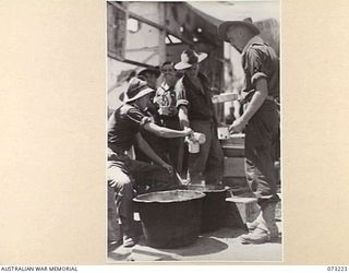 ALEXISHAFEN, NEW GUINEA. 1944-05. MEMBERS OF THE 2/15TH FIELD AMBULANCE BEING SERVED DURING THE MID DAY MESS PARADE AT THEIR CAMP SITE IN THE OLD CATHOLIC MISSION. IDENTIFIED PERSONNEL ARE:- ..