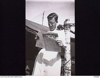 CAPE WOM, WEWAK AREA, NEW GUINEA. 1945-09-01. PRIVATE E.J. MITCHELL, 2/4 DENTAL UNIT ATTACHED HEADQUARTERS 6 DIVISION READING THE ARMY NEWSPAPER GUINEA GOLD DURING A BREAK