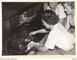 LAE, NEW GUINEA. 1945-11-08. LANCE CORPORAL E. HUMBERG, AUSTRALIAN WOMEN'S ARMY SERVICE INSTRUCTOR (1) WITH SERGEANT B.L. WARD (2), AND SIGNALWOMAN CHURCH (3) BASTING A ROAST LEG OF MUTTON DURING ..