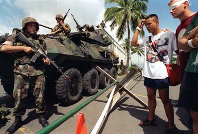 US Marine Corps Lance Corporal (LCPL) Doy Gorton armed with the M16A2 assault rifle and Marines atop a Light Assault Vehicles (LAV-25) guard wounded civilians inside a barricaded area during the simulated Noncombatant Evacuation Operation (NEO) at Kaneohe Bay Marine Corps Station, HI. Part of Operation RIMPAC 96, Marines from the 11th Marine Expeditionary Unit (MEU) Camp Pendleton, CA conducted training exercises in the evacuation of civilians from hostile environments