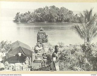 JACQUINOT BAY, NEW BRITAIN. 1944-11-16. AUSTRALIAN TROOPS AND NATIVES UNLOADING SUPPLIES FROM BARGES AT THE BEACH-HEAD OF THE 5TH BASE SUB AREA IN THE PALMALMAL PLANTATION