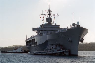 A starboard bow view of the USS BLUE RIDGE (LCC 19) being assisted by two tugboats while docking at the Sierra Pier, Guam during Exercise TANDEM THRUST 99