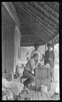 Medical assistant looking through microscope, two men look on, Yule Island