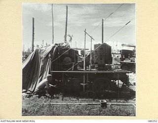 HANSA BAY, NEW GUINEA. 1944-07-10. A MEMBER OF THE 5TH DIVISION SALVAGE GROUP EXAMINES A 2' 6" SEARCHLIGHT ON AN ABANDONED JAPANESE TRUCK. ITS 110 VOLT DC GENERATING PLANT AT PRESENT SUPPLIES LIGHT ..