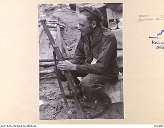 BOUGAINVILLE. 1945-05-21. CORPORAL G. REED, 58/59 INFANTRY BATTALION, EXAMINING A .303 INCH RIFLE WITH ITS WOODWORK SPLIT BY JAPANESE ARTILLERY. HE DIVED FOR COVER WHEN THE ARTILLERY OPENED UP AND ..