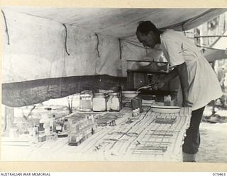 MILILAT, NEW GUINEA. 1944-08-23. NX166337 CORPORAL E.G. BLAKE, DENTAL ORDERLY, ARRANGING THE INSTRUMENTS AND STERILISER IN THE TENT DENTAL SURGERY OF THE 77TH DENTAL UNIT