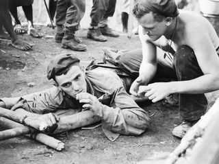 BOUGAINVILLE ISLAND. 1944-12-31. Q21632 CORPORAL L. BENTLEY GIVING A CIGARETTE TO NX193389 PRIVATE R.C. MALE, 25TH INFANTRY BATTALION, WHO WAS WOUNDED DURING THE AUSTRALIAN ATTACK ON JAPANESE ..