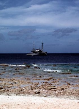 The salvage ship USS BOLSTER (ARS 38) prepares to set anchor offshore of the island