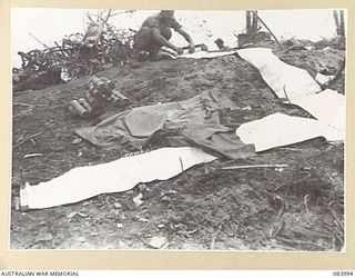 BOUGAINVILLE, SOLOMON ISLANDS. 1944-12-13. CORPORAL D E JORGENSON, 9 INFANTRY BATTALION, ROLLING AIR INDICATOR STRIPS ON LITTLE GEORGE HILL AT THE CONCLUSION OF AN AIR STRIKE AGAINST ARTILLERY HILL