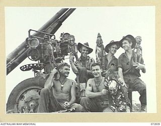 ALEXISHAFEN, NEW GUINEA. 1944-04-30. MEMBERS OF THE 30TH INFANTRY BATTALION, GROUPED BESIDE A 77MM JAPANESE FIELD ANTI-AIRCRAFT GUN, ON THE FORESHORE, HOLD WOODEN NATIVE CARVINGS WHICH WERE ..