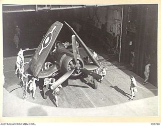 AT SEA OFF RABAUL, NEW BRITAIN. 1945-09-06. A CORSAIR AIRCRAFT BEING WHEELED INTO THE LIFT ON THE HANGAR DECK OF THE AIRCRAFT CARRIER HMS GLORY TO GO UP TO THE FLIGHT DECK FOR TAKEOFF. CORSAIRS ..