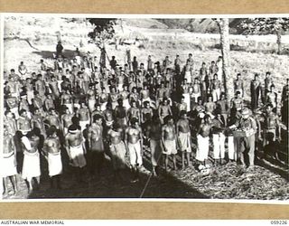 KUMBARUM, NEW GUINEA, 1943-10-23. GROUP OF NATIVE BOYS RECEIVING THEIR RATION OF TOBACCO AND MATCHES AT THEIR EVENING LINE UP AT HEADQUARTERS, 7TH AUSTRALIAN DIVISION AREA