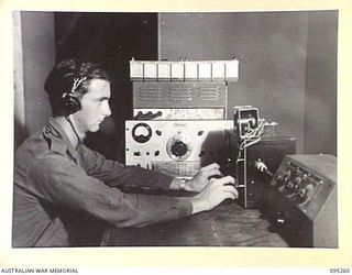 JACQUINOT BAY, NEW BRITAIN, 1945-08-12. SERGEANT N.P. GILCHRIST IN THE CONTROL ROOM OF THE NEW RADIO STATION 9AE, OPERATED BY AUSTRALIAN ARMY AMENITIES SERVICE. HE IS ATTEMPTING TO PICK UP ANY NEWS ..