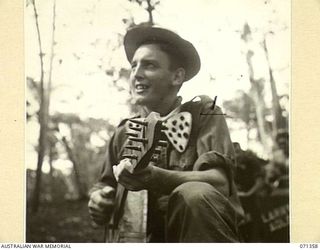 GUSIKA, NEW GUINEA, 1944-03-17. V125901 PRIVATE W. ROBINS, 29/46TH INFANTRY BATTALION, 4TH INFANTRY BRIGADE, PLAYS A SPANISH GUITAR MADE FROM A BISCUIT TIN. HE IS A MEMBER OF "TRENKNER'S TROUBADOUR ..