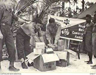 PALMALMAL PLANTATION, NEW BRITAIN. 1944-12-25. AUSTRALIAN COMFORTS FUND PERSONNEL UNPACKING CHRISTMAS HAMPERS AT HEADQUARTERS, 5TH DIVISION. LEFT TO RIGHT ARE: PRIVATE S. R. KENCHINGTON; PRIVATE A. ..