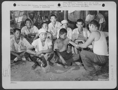 Cpl. Roy Cole, Medical Man, Dresses Wounds Of One Of The Korean Prisoners-Of-War As A Guard Looks On. Cpl. Cole Is From Iowa Park, Texas. Saipan, Marianas Islands, 6 July 1944. (U.S. Air Force Number 63722AC)