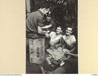 1943-09-14. NEW GUINEA. KOMIATUM RIDGE. MEMBERS OF THE A.I.F. PLAYING CARDS AFTER THEY HAD DRIVEN THE JAPANESE FROM KOMIATUM RIDGE. SITTING ON THE CASE WITH JAPANESE LETTERING IS PTE. WALLY FORD, ..