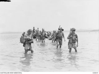 PAPUA, NEW GUINEA. 1942-07. MEMBERS OF AN AUSTRALIAN INFANTRY PATROL WADING ASHORE AFTER HAVING BEEN TRANSPORTED BY A NATIVE "LAKATOI" ACROSS THE MOUTH OF A RIVER WHILST ON A COASTAL PATROL