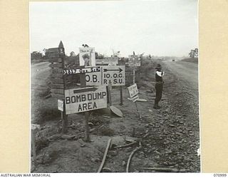 NADZAB, NEW GUINEA, 1944-03-09. THE PROVOST ON DUTY AT THE APPROACH TO THE NADZAB AIRSTRIP NEAR A HOST OF SIGNS POINTING TO UNITS IN THE AREA