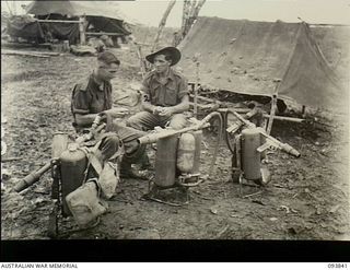 Yamil, New Guinea. 1945-07-06. VX24879 Private F.G. Jones (on the left) and VX8470 Private R.L. Picone of D Company, 2/5th Australian Infantry Battalion, relaxing beside their flame throwers. Half ..