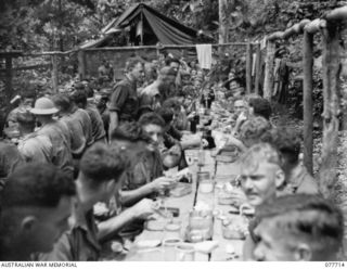 BOUGAINVILLE ISLAND. 1944-12-25. TROOPS OF THE 9TH INFANTRY BATTALION ENJOYING CHRISTMAS DINNER CONSISTING OF SOUP, TURKEY, HAM, ROAST POTATOES, PEAS, CHRISTMAS PUDDING, CUSTARD AND BEER